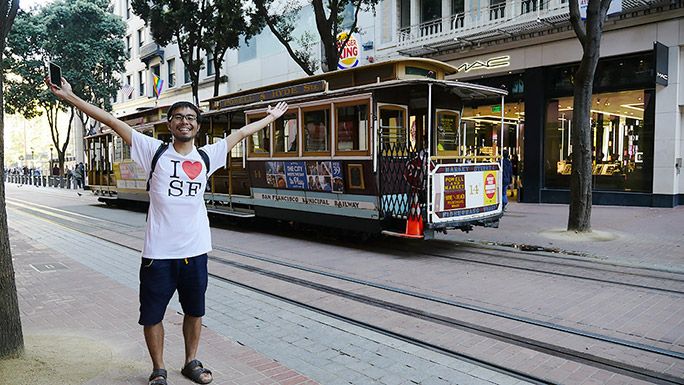新しく買ったTシャツを着て路面電車の前でポーズをする地主
