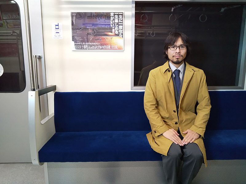 電車を模したスタジオにてカメラ目線で映る地主
