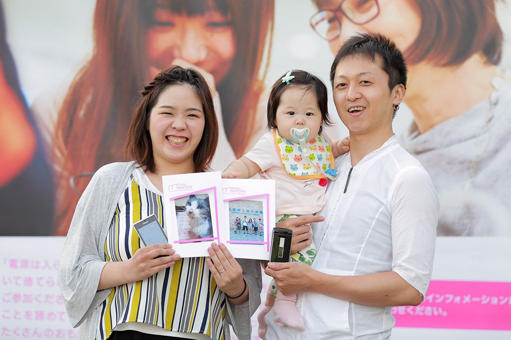 「おもいでケータイ再起動」でプリントした写真を手に微笑む夫婦と子ども