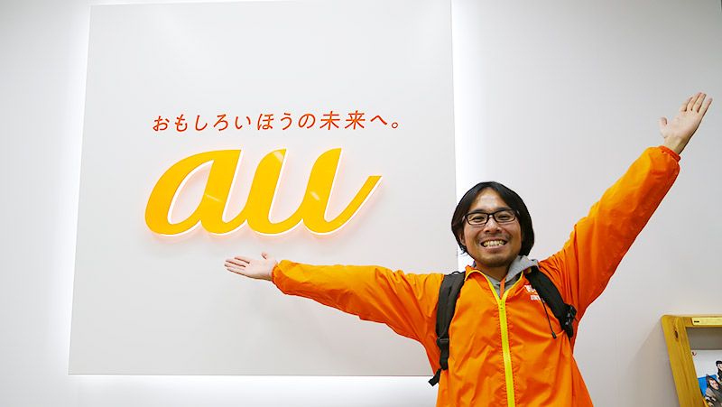 auのロゴの前に立つ地主恵亮