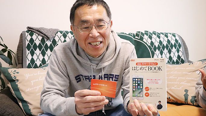auスマートサポートのカードと加入特典の「はじめてBOOK」を持つ父