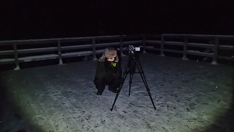 三脚を立てて雪原でオーロラをしゃがみながら待つ地主