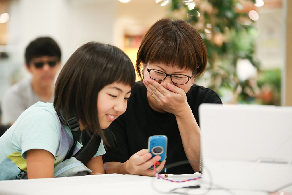 「おもいでケータイ再起動」でガラケーが復活し喜ぶ女性と子どもたち