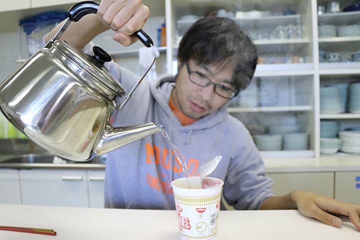 やかんから沸騰したお湯をカップラーメンに注ぐライターの地主