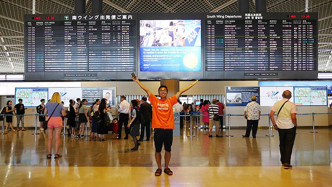 空港の出発便案内の前に立ち、ポーズを決める地主