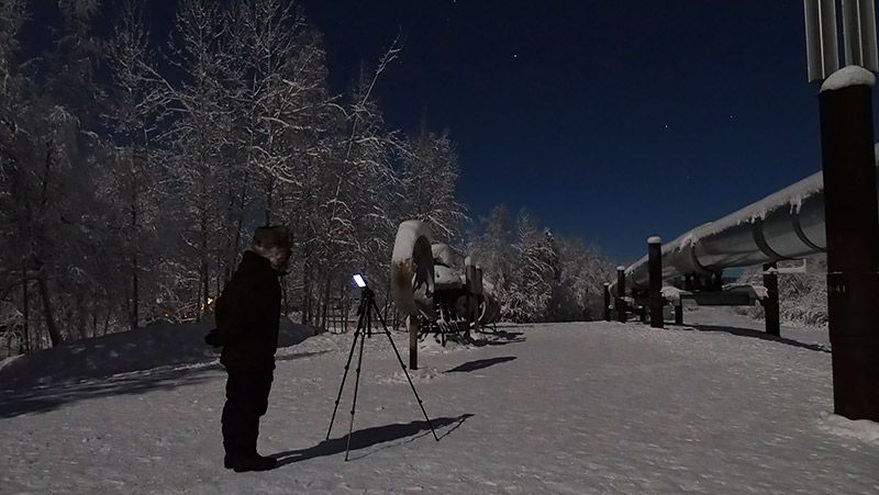 雪原にTORQUE G03を立てた三脚をのぞく地主