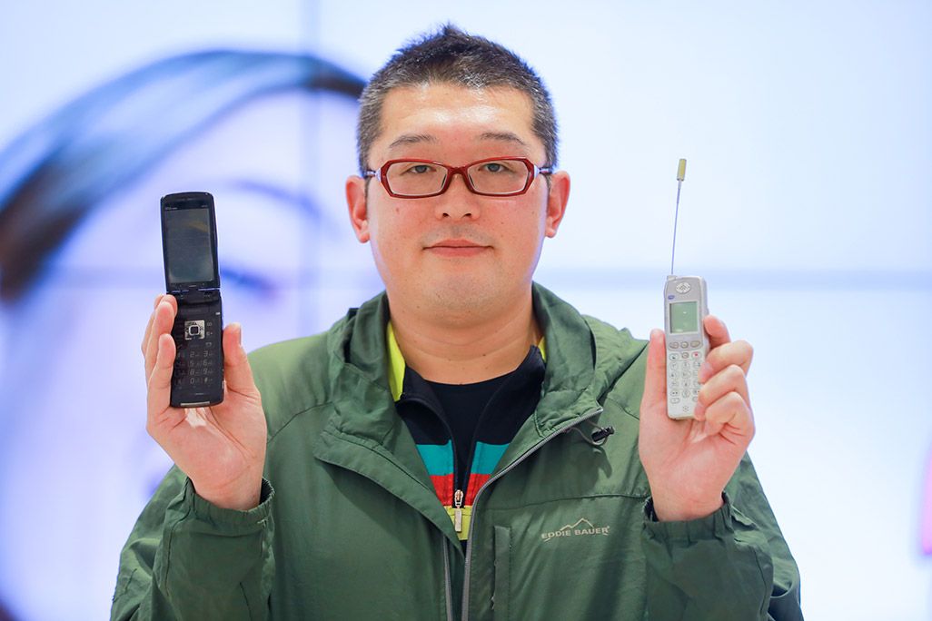 au 昔のケータイを2台持ち、微笑む男性