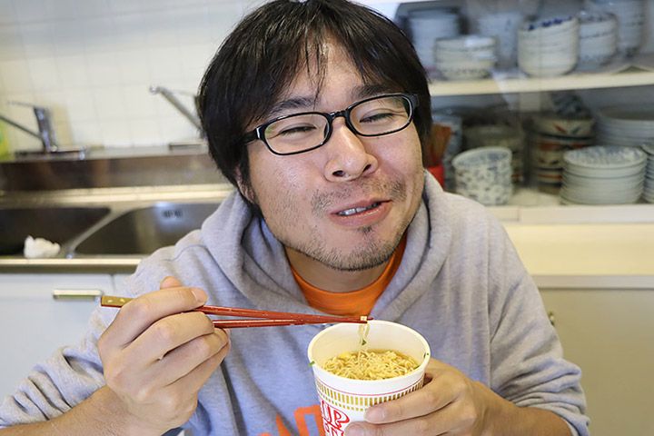 カップラーメンをほおばり、笑顔を浮かべるライターの地主