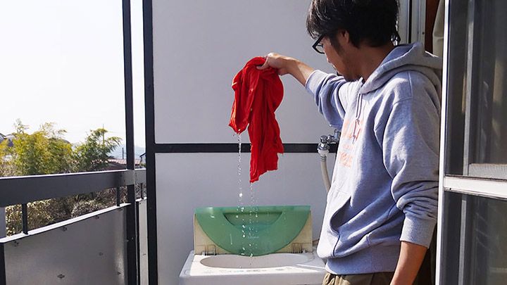 洗濯機からびちょびちょのTシャツを取り出すライターの地主