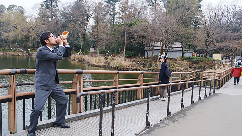 法螺貝を吹く地主を振り返って見つめるAさん